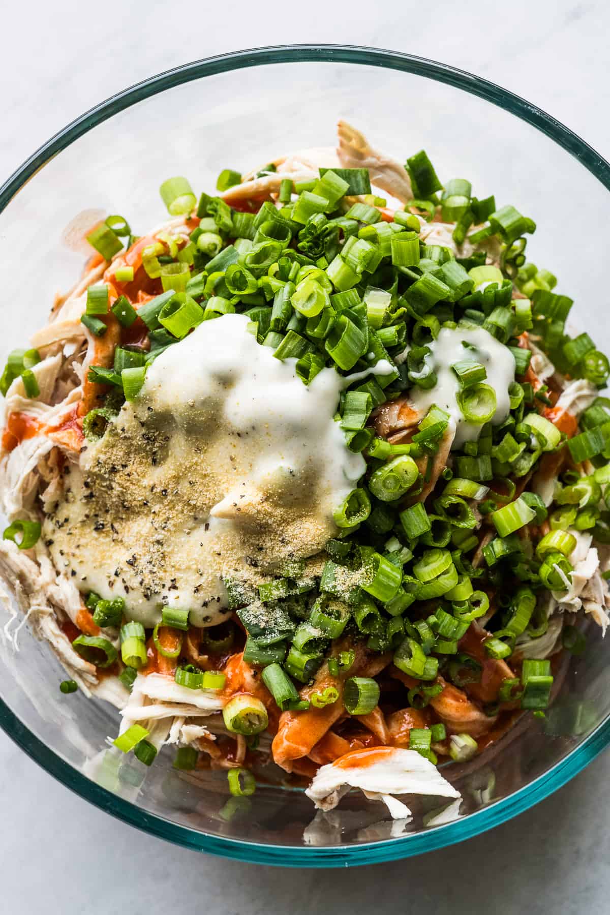 Shredded chicken, buffalo sauce, green onions, ranch dressing in a bowl.