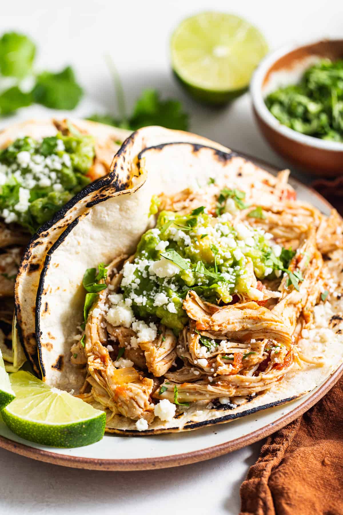 Crockpot chicken tacos served with guacamole and cotija cheese.