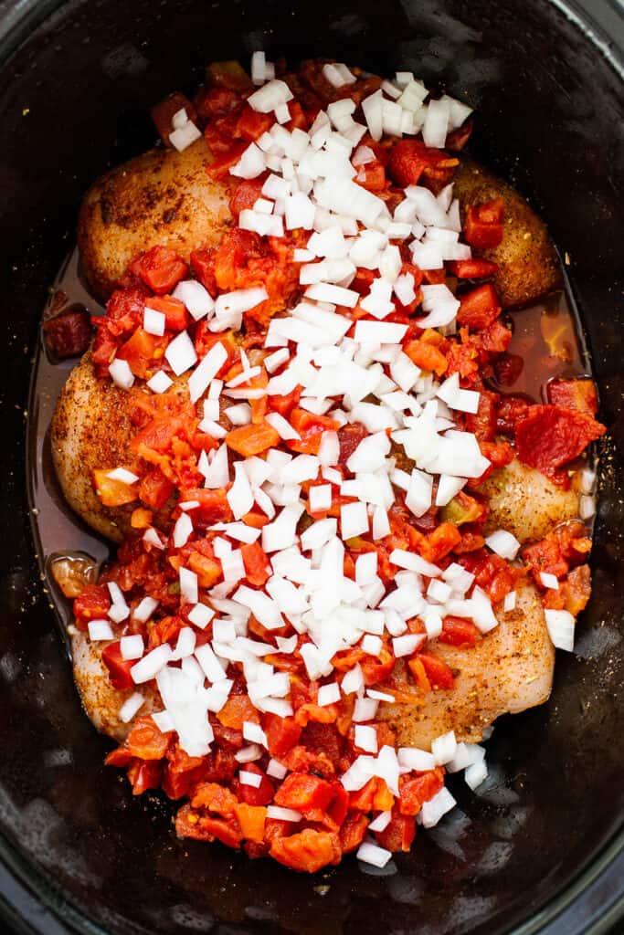 Chicken breasts, canned tomatoes, onion, and taco seasoning in a crockpot.