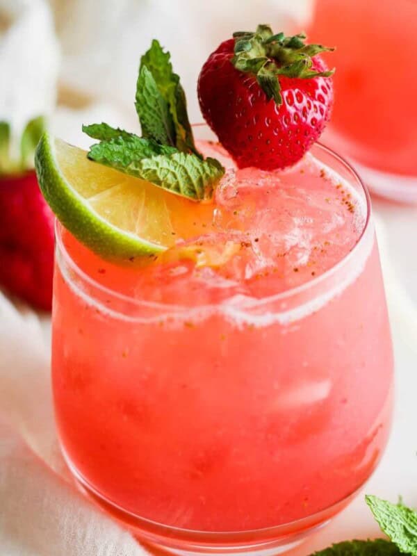 Agua de fresa (strawberry agua fresca) in a glass garnished with mint leaves, a lime wedge, and a fresh strawberry.