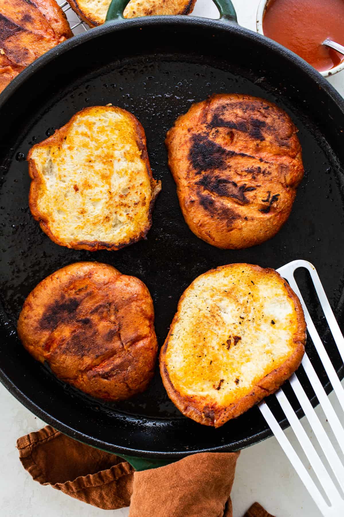 Telera bread being pan-fried in a skillet with a red chile sauce.