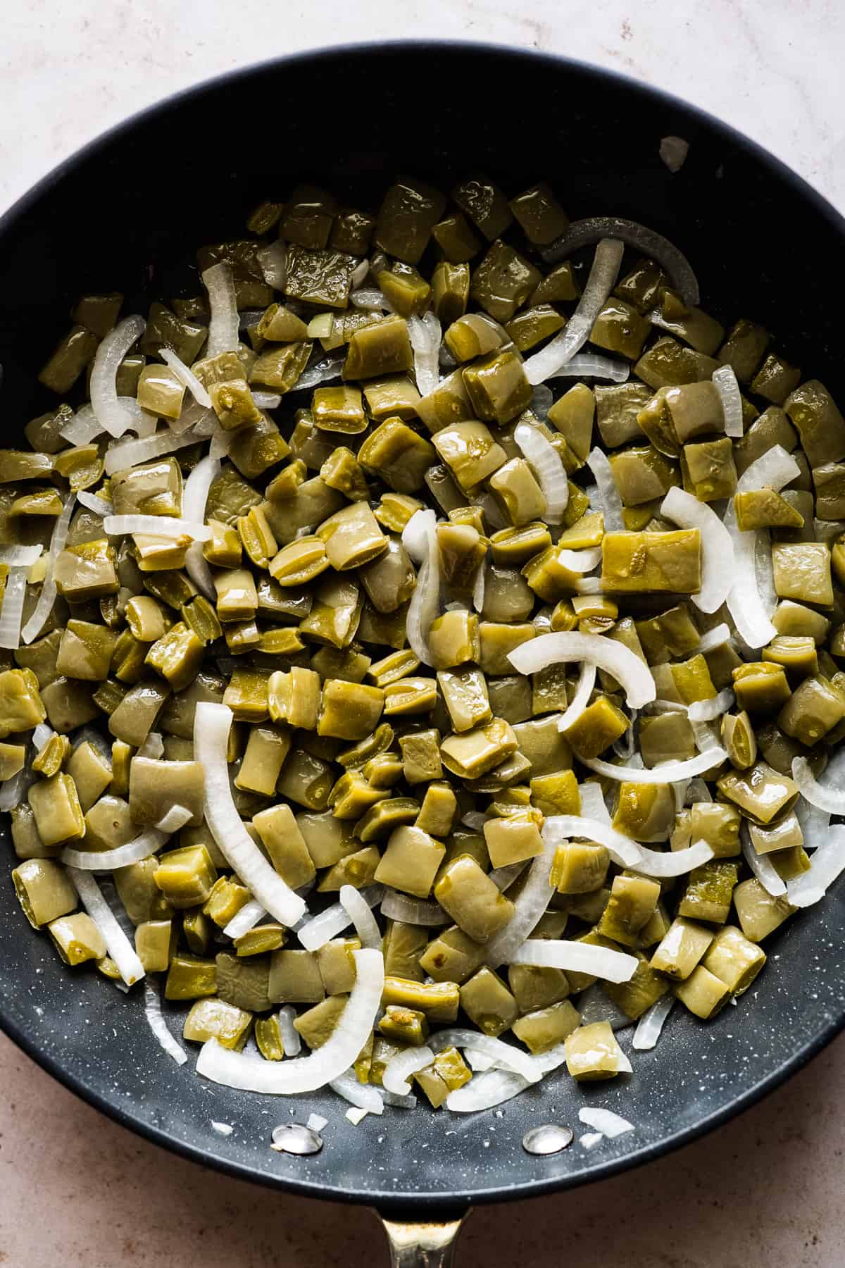 Cooked nopales and sliced onions in a skillet.