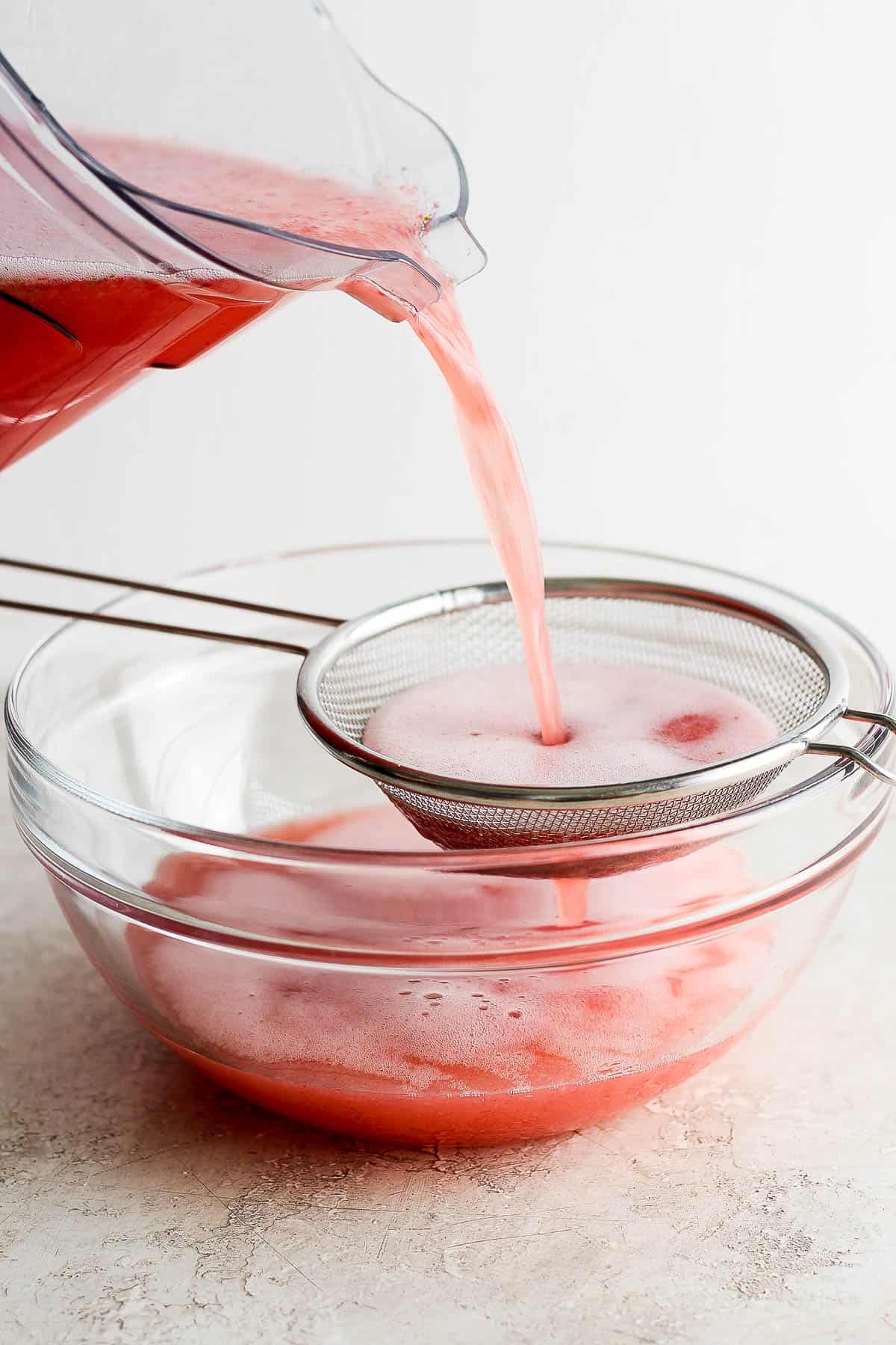 Agua de fresa (strawberry agua fresca) being poured through a strainer.