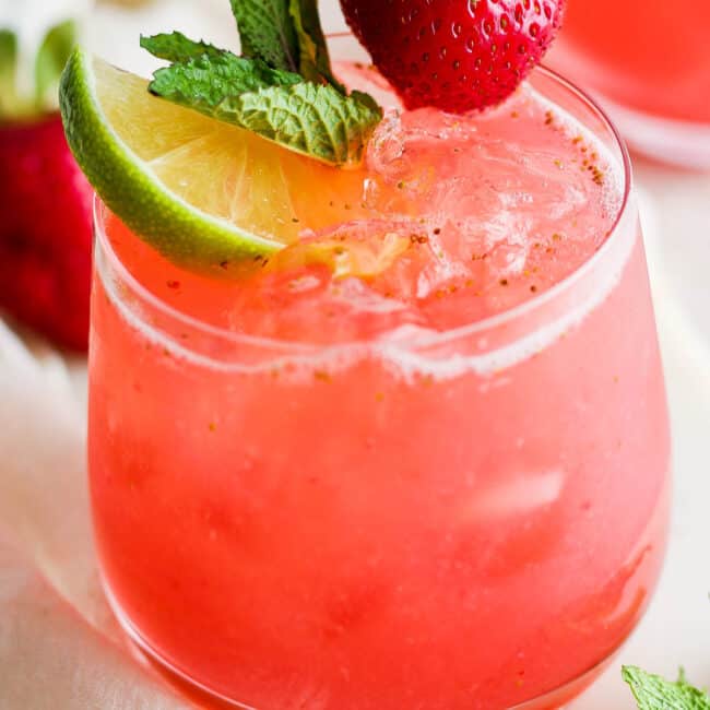 Agua de fresa (strawberry agua fresca) in a glass garnished with mint leaves, a lime wedge, and a fresh strawberry.