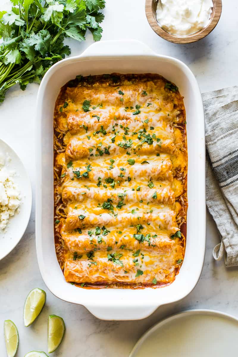 Red chicken enchiladas in a baking dish with melted cheese and chopped cilantro.