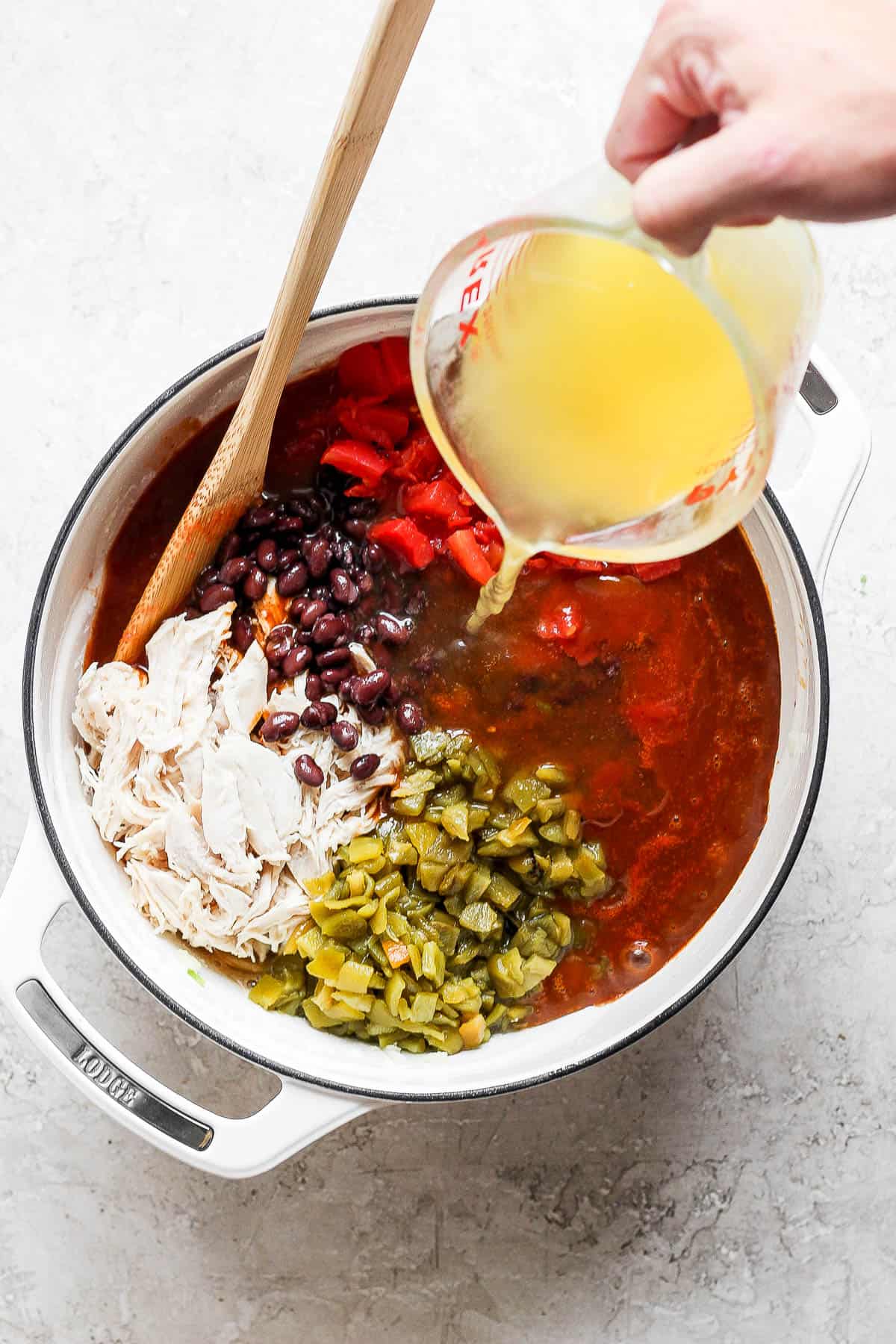 Broth being poured into a pot of chicken enchilada soup.