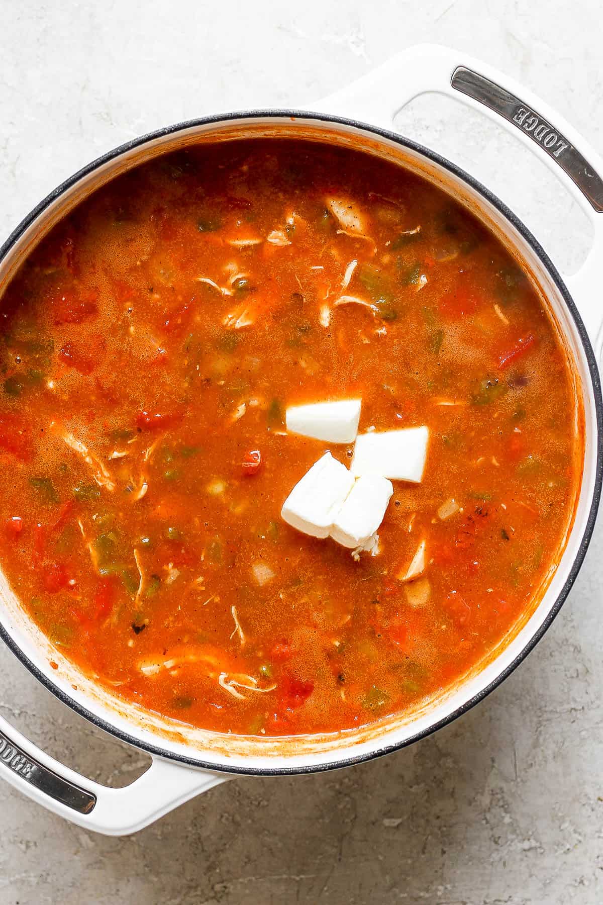 Cream cheese in a pot of chicken enchilada soup before being stirred in.