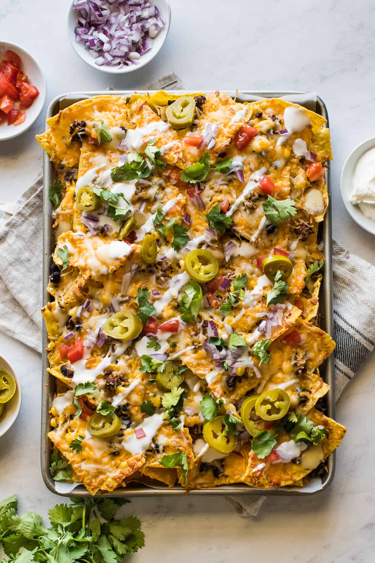 Sheet pan nachos topped with sour cream, jalapeños, tomatoes, and diced onion.