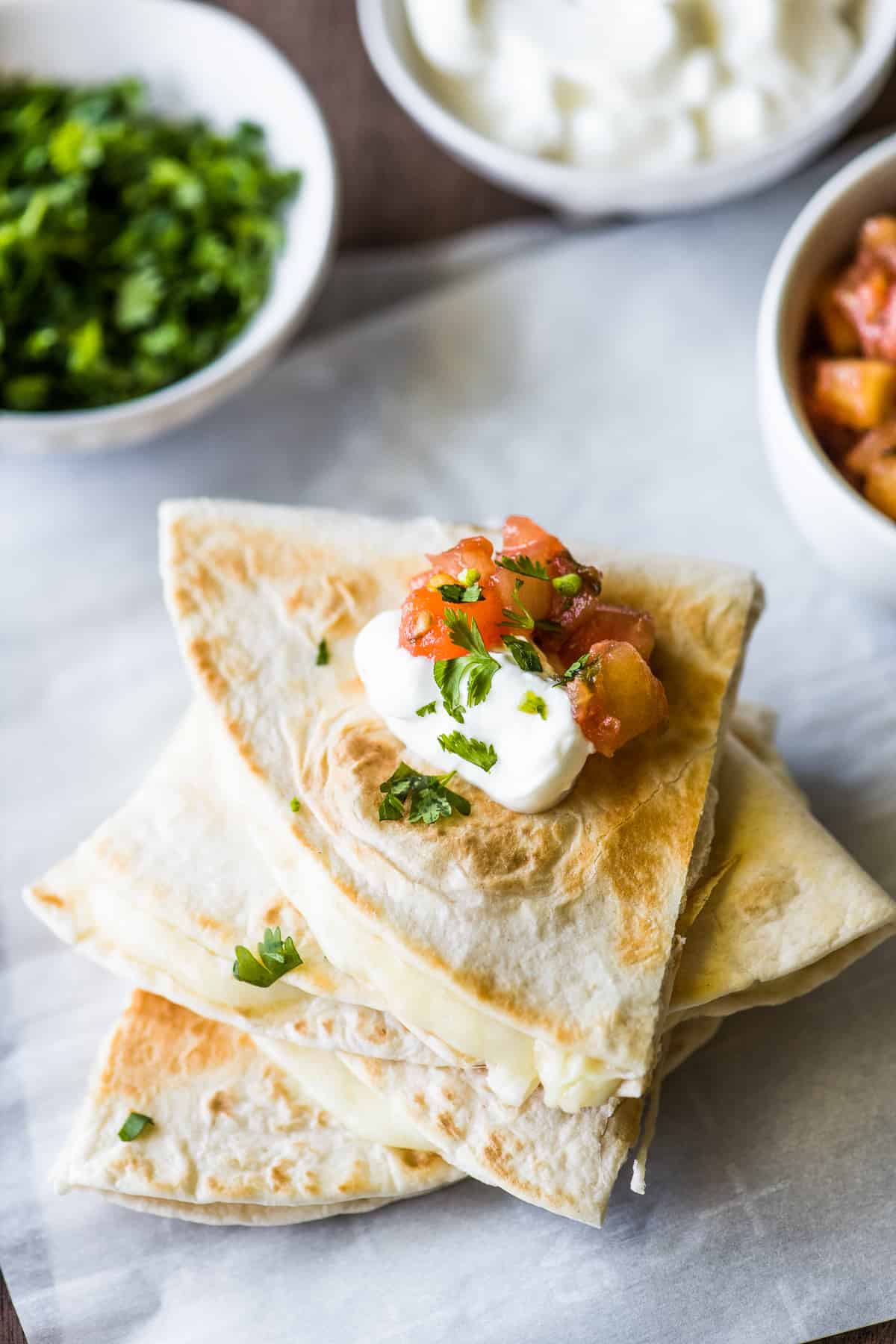 Cheese quesadillas sliced and stacked on top of each other with sour cream and pico de gallo
