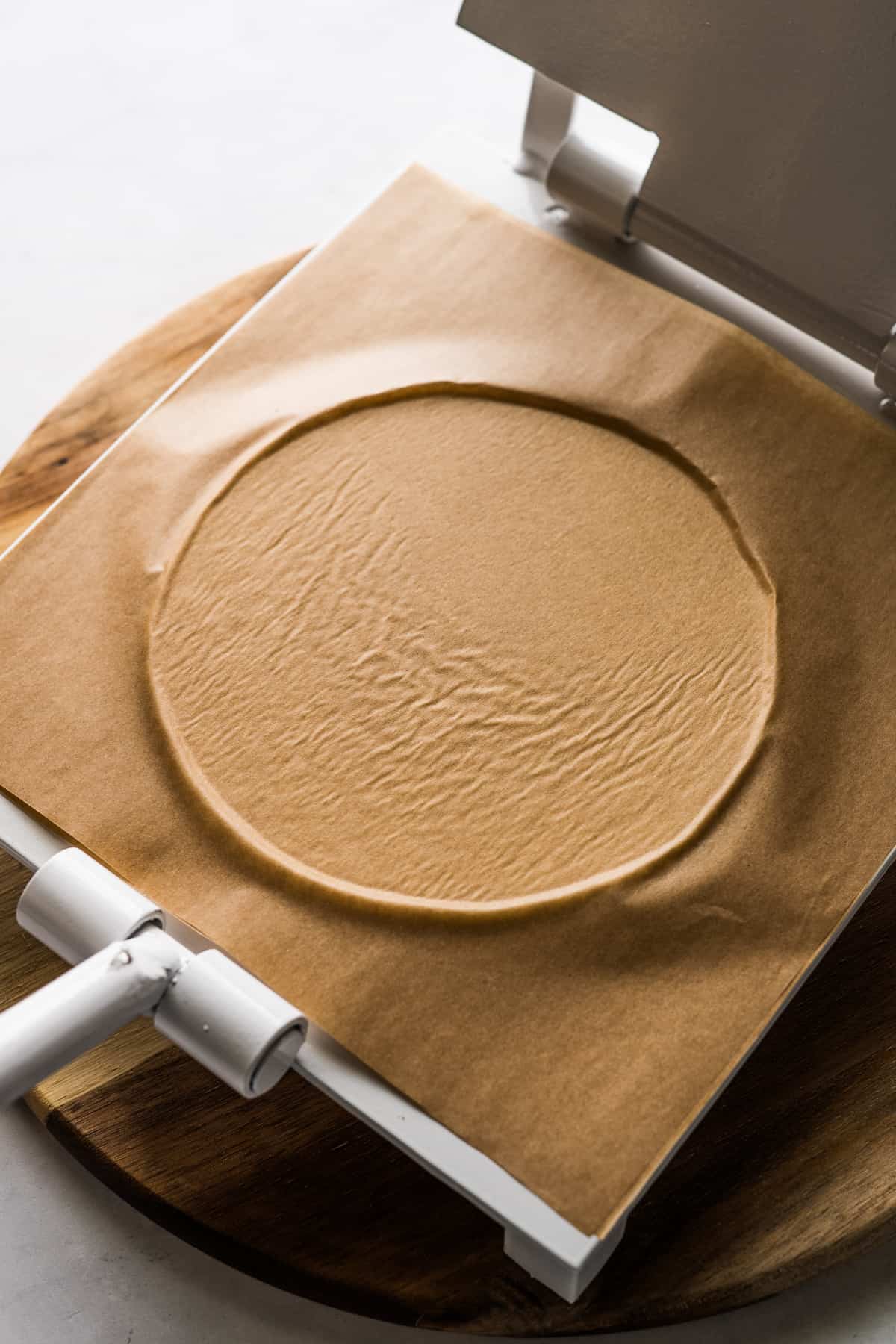 A flattened ball of masa covered with parchment paper on a tortilla press.