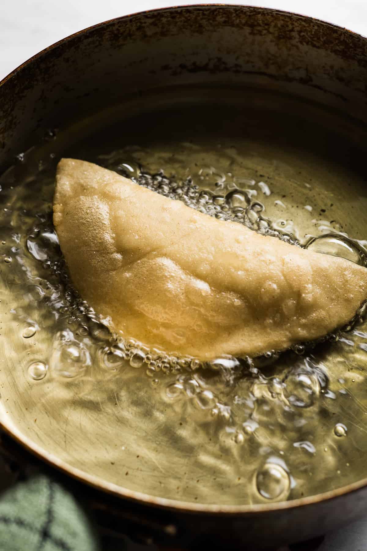 A quesadilla being fried in a deep skillet in oil.