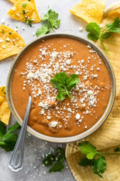 Frijoles puercos in a bowl topped with cotija cheese and served with tortilla chips.