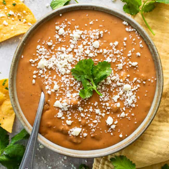 Frijoles puercos in a bowl topped with cotija cheese and served with tortilla chips.