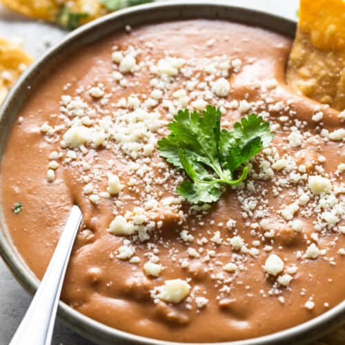 Frijoles puercos in a bowl garnished with cotija cheese and cilantro.