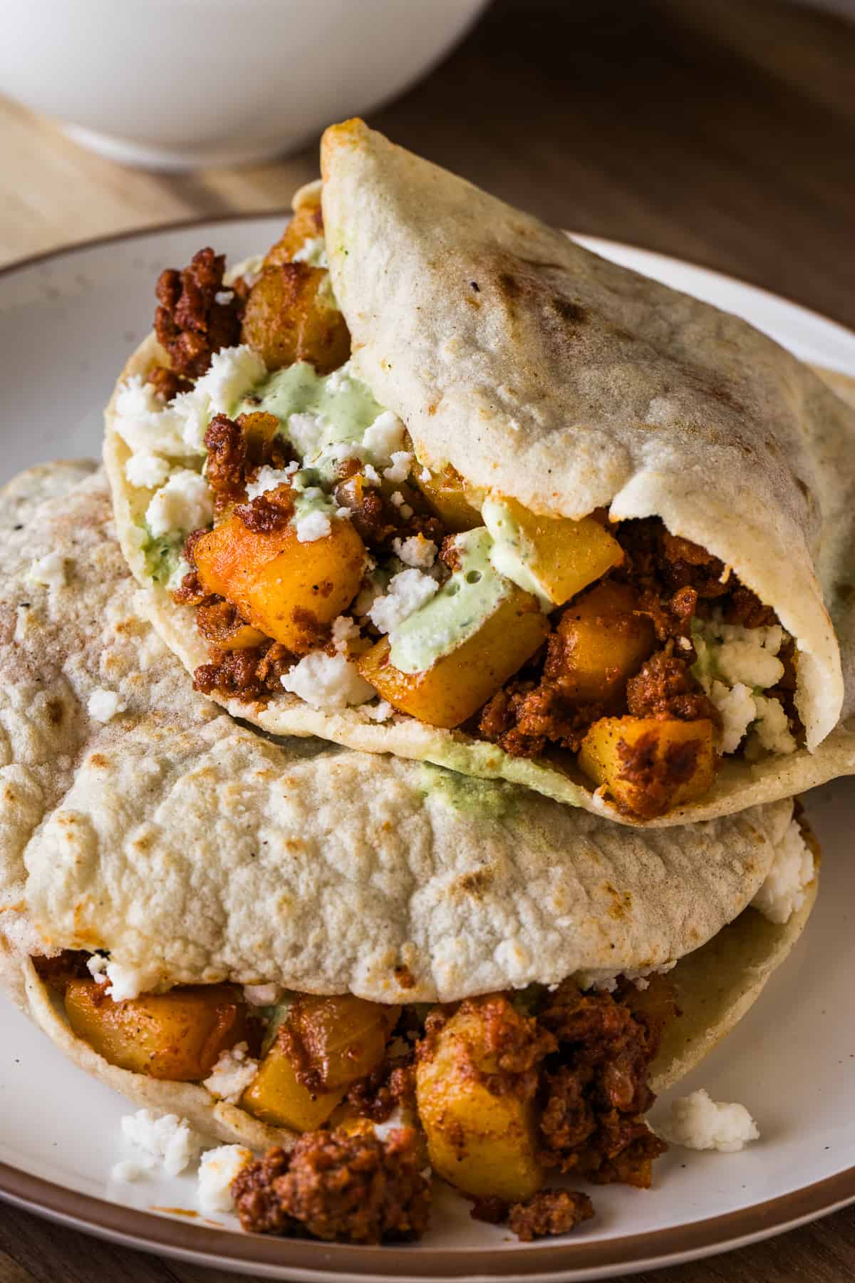 Gorditas stacked on top of one another filled with papas con chorizo and garnished with queso fresco and cilantro lime crema.