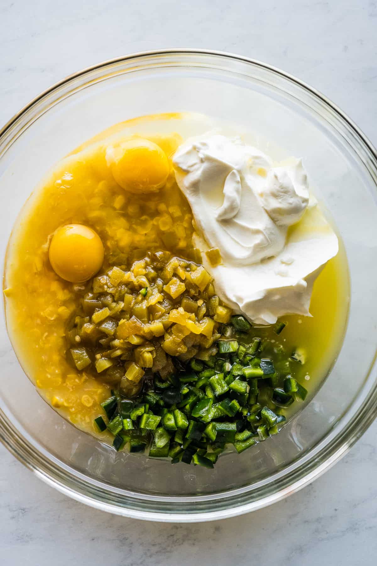 Eggs, corn, creamed corn, diced green chiles, and sour cream in a bowl.