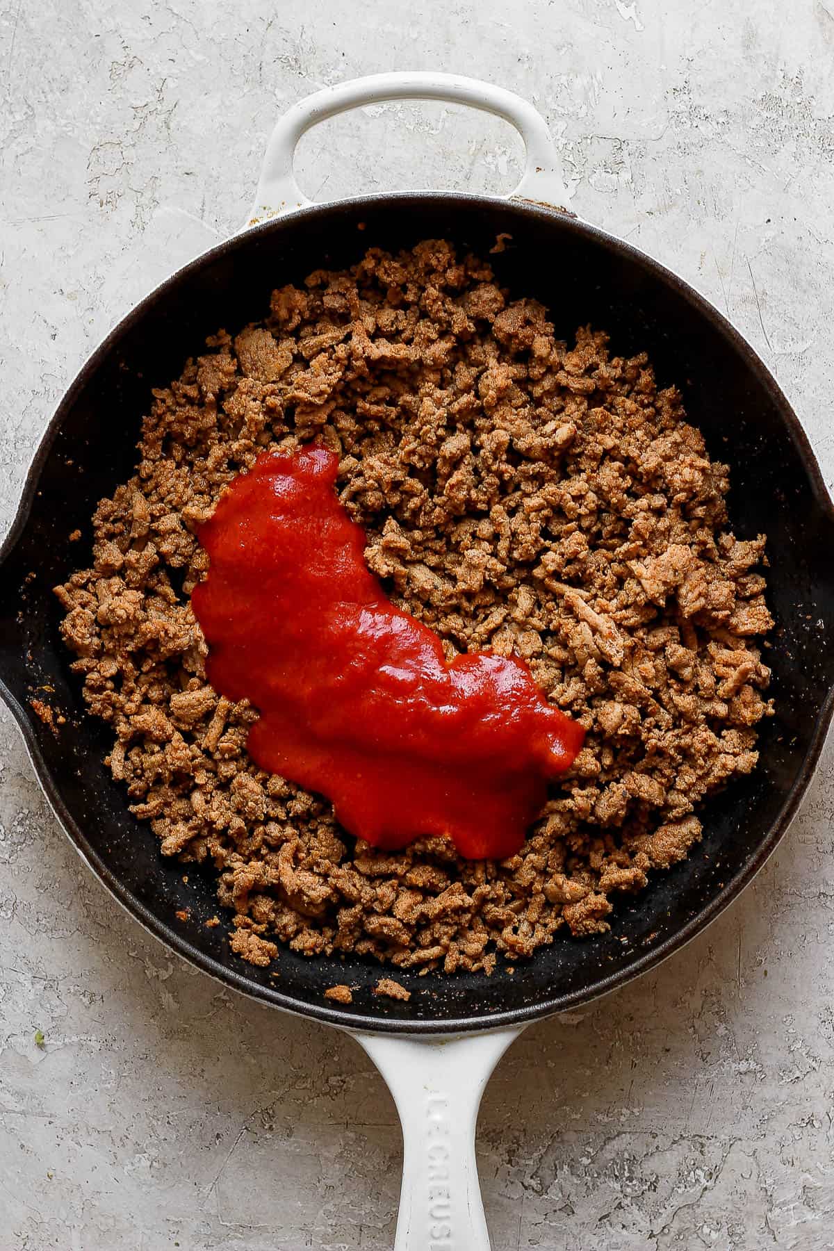 Ground turkey in a skillet with tomato sauce poured in.