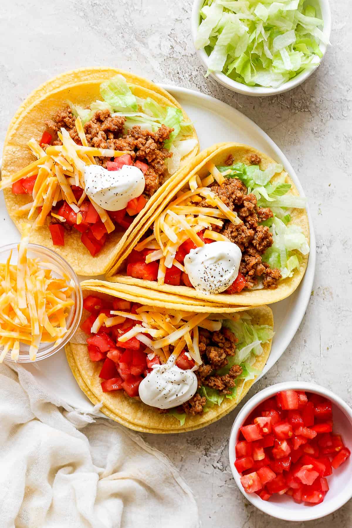 Ground turkey tacos on a plate served with lettuce, tomatoes, cheese, and sour cream.