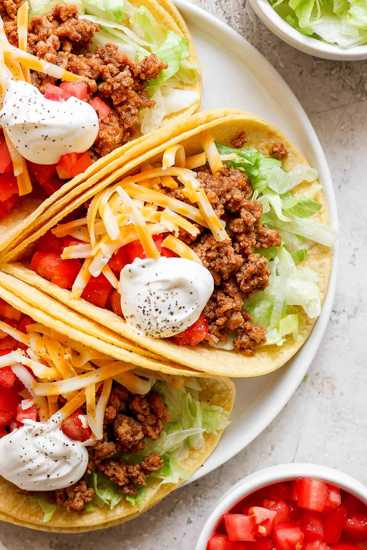 Ground turkey tacos on a plate garnished with shredded cheese, diced tomatoes, lettuce, and sour cream.