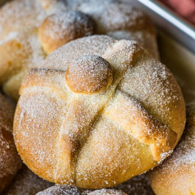 Pan de Muerto on a baking sheet rolled in cinnamon.