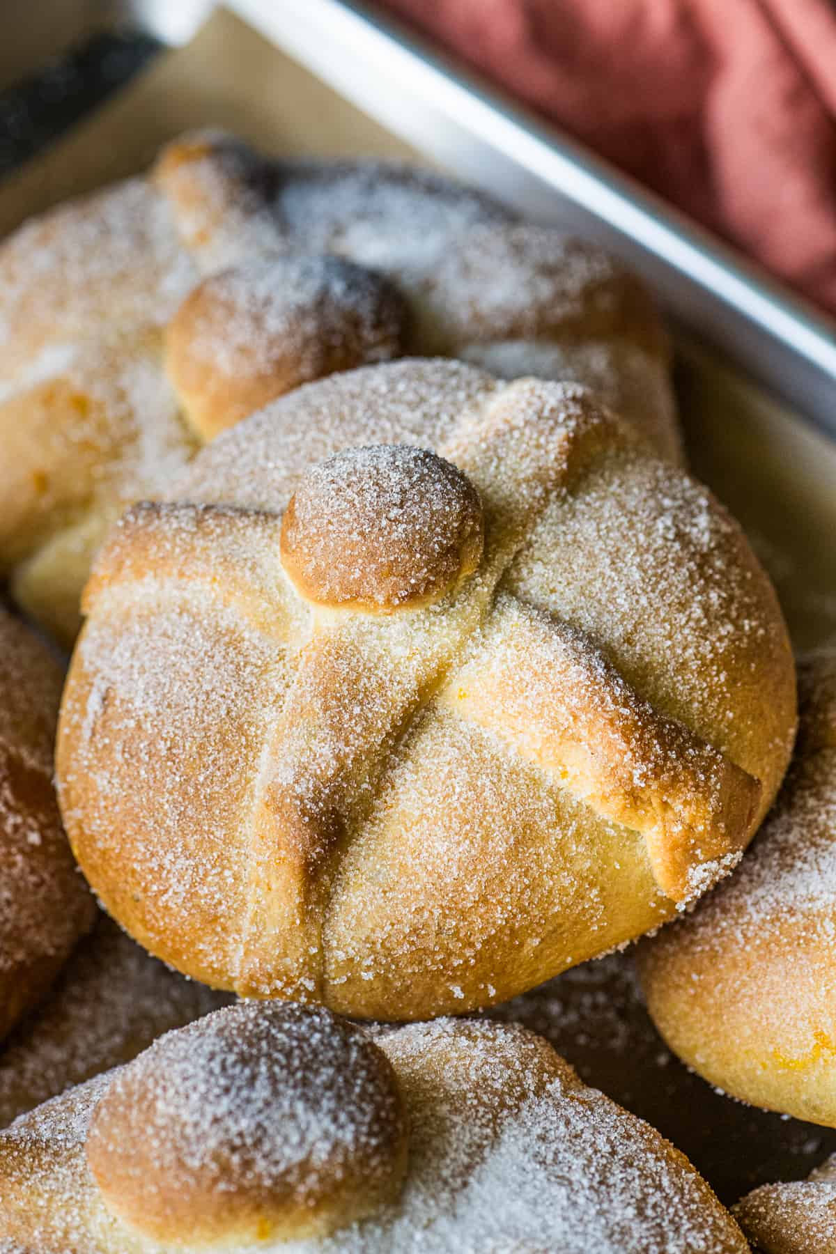 Pan de Muerto on a baking sheet rolled in cinnamon.