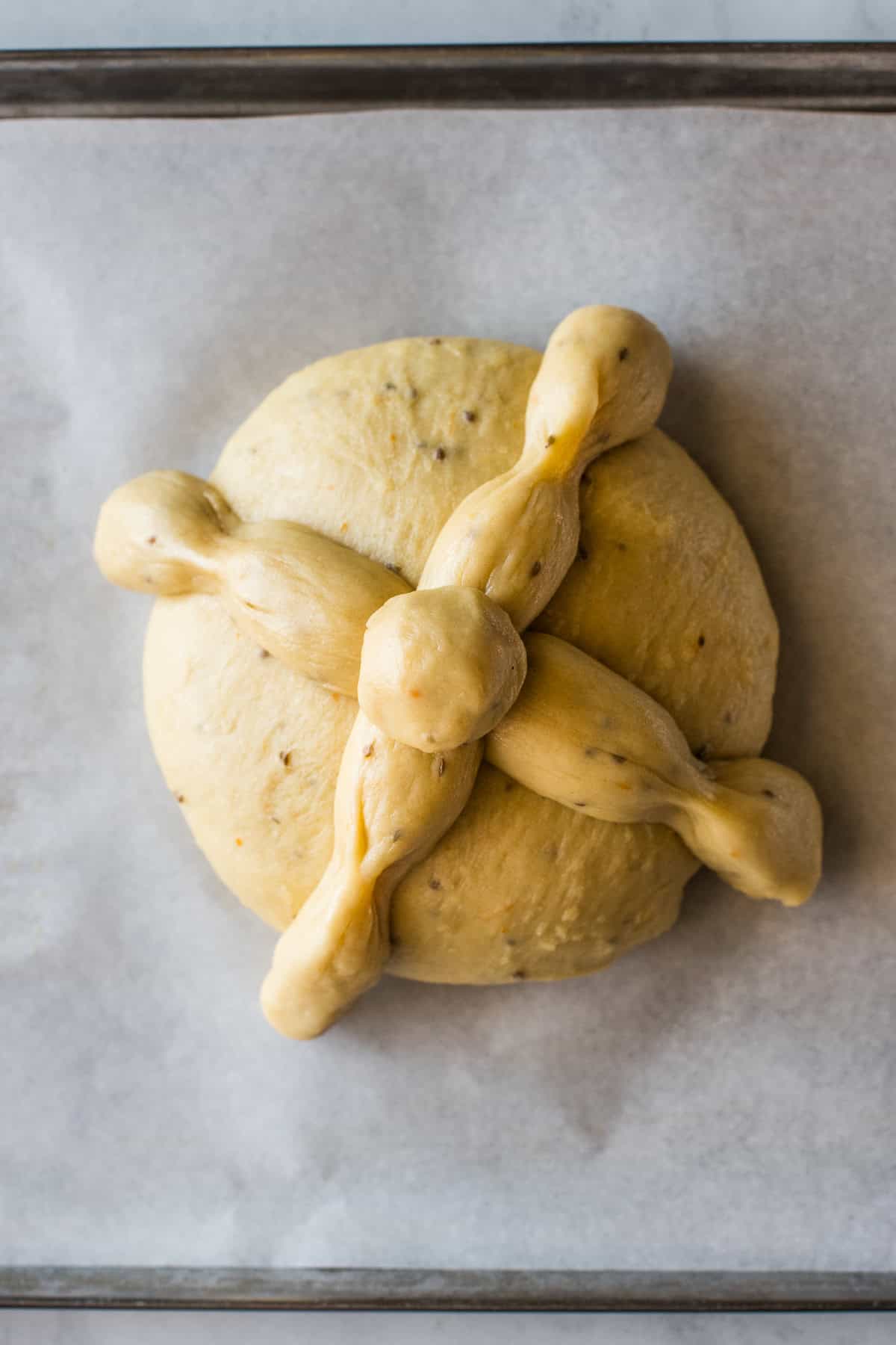 Shaped pan de muerto on a baking sheet lined with parchment paper before being baked.