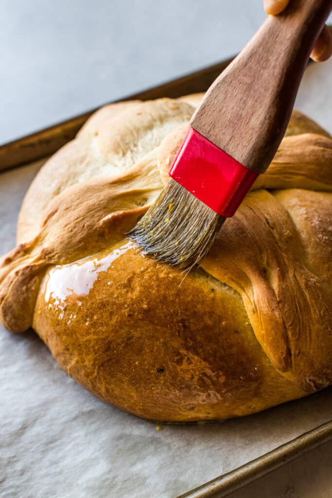 A loaf of pan de muerto being brushed with melted butter.