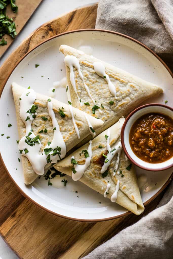 Tetelas on a plate served with Mexican crema, salsa, and chopped cilantro.