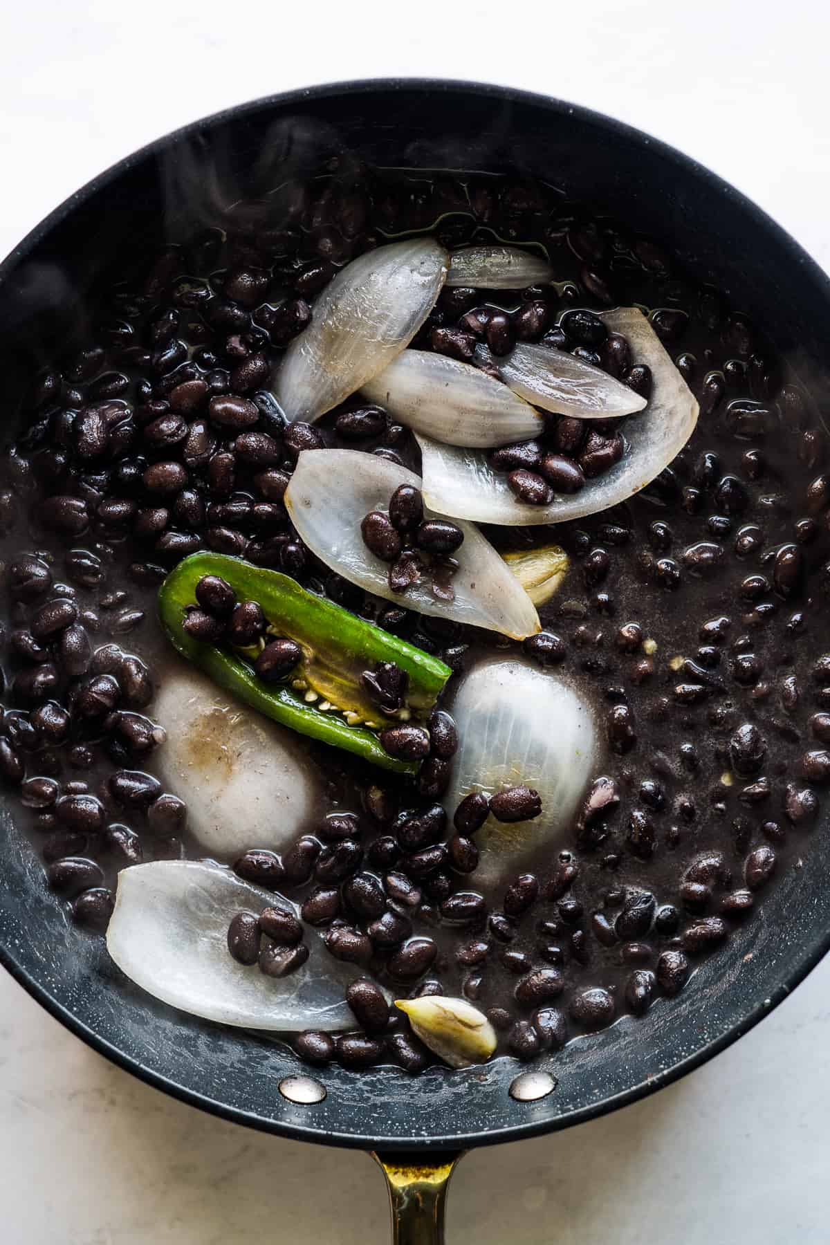 Black beans, onion, jalapeño, and garlic cooking in a skillet.