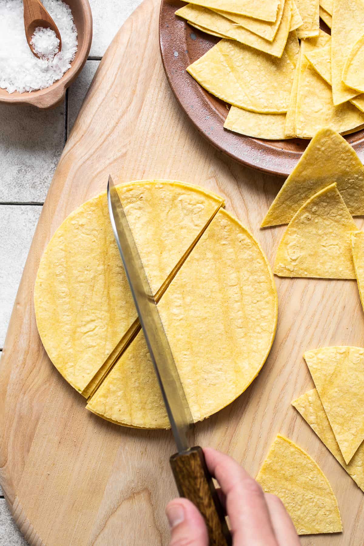 Corn tortillas on a cutting board being sliced into triangles for tortilla chips.