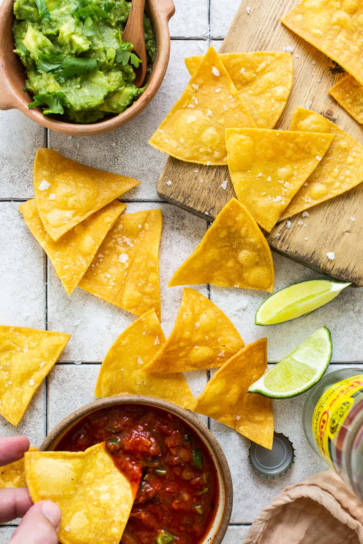 Homemade tortilla chips on a table with guacamole and salsa.