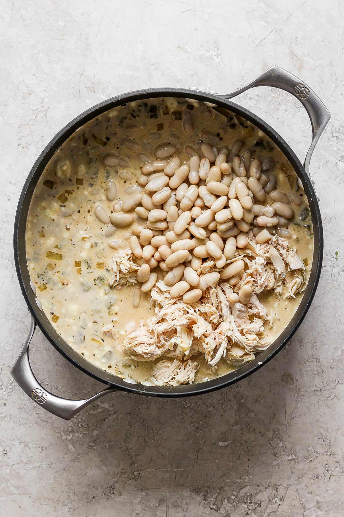 Cannellini beans being stirred into a pot of white chicken chili;
