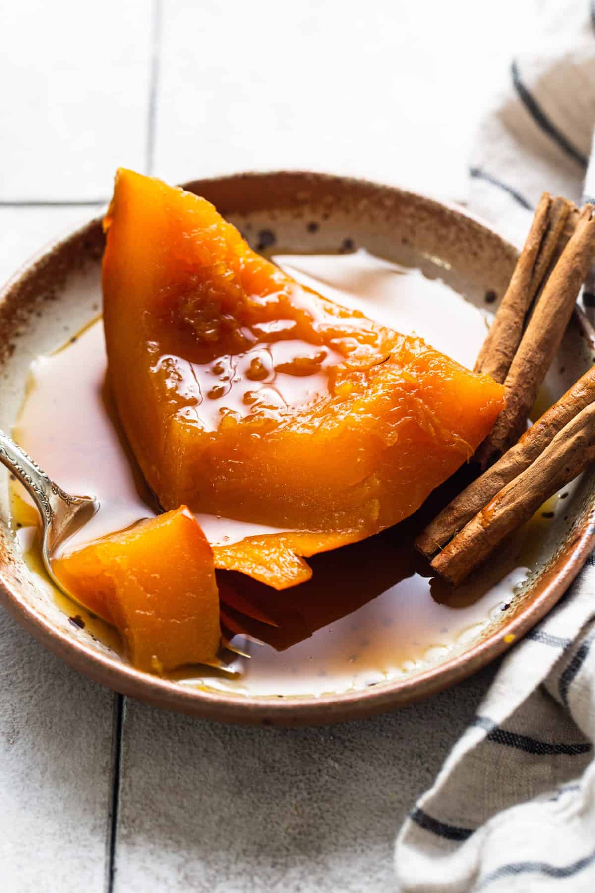 A slice of tender calabaza en tacha on a plate served with a piloncillo syrup.