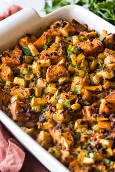 A baking dish of chorizo stuffing garnished with fresh parsley and made with apples, onion, and celery.