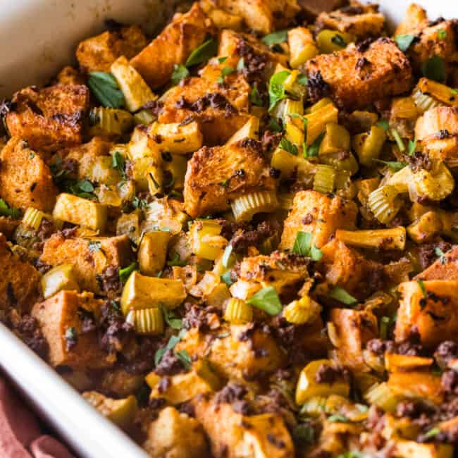 A baking dish of chorizo stuffing garnished with fresh parsley and made with apples, onion, and celery.