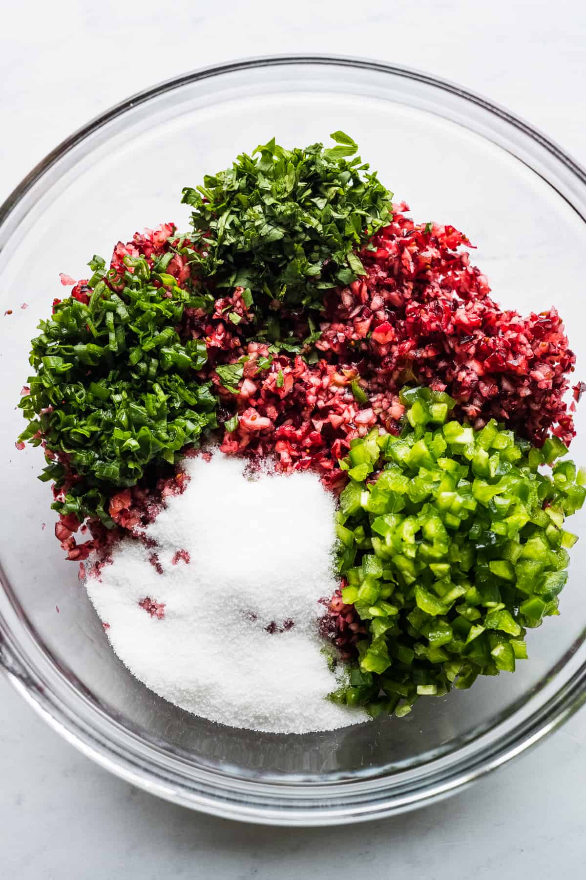 Finely chopped cranberries in a bowl with cilantro, sugar, green onions, jalapeños, orange juice, and lime juice.