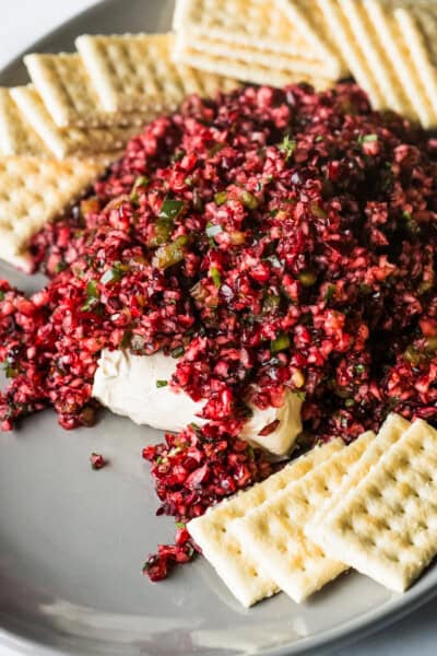 Cranberry salsa on a serving plate on top of a block of cream cheese with some crackers on the side.