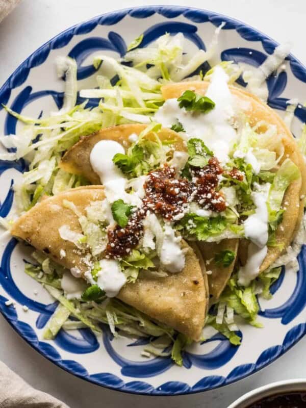 Tacos dorados on a plate served with shredded lettuce, Mexican crema, and a roasted tomato salsa.