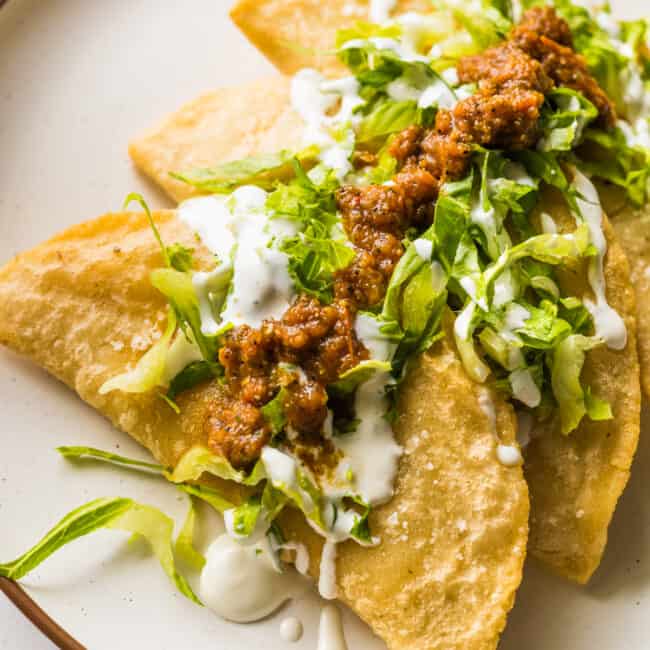 Fried quesadillas (quesadillas fritas) on a plate topped with lettuce, salsa, and Mexican crema.