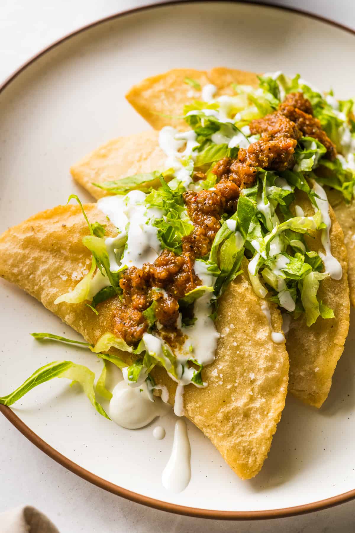 Fried quesadillas (quesadillas fritas) on a plate topped with lettuce, salsa, and Mexican crema.