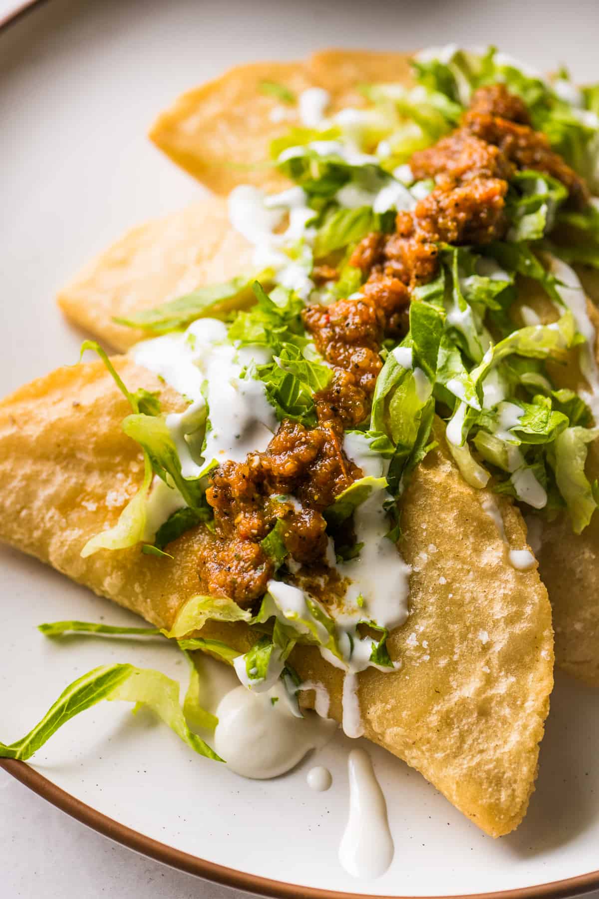 Golden and crispy fried quesadillas garnished with lettuce, Mexican crema, and salsa.