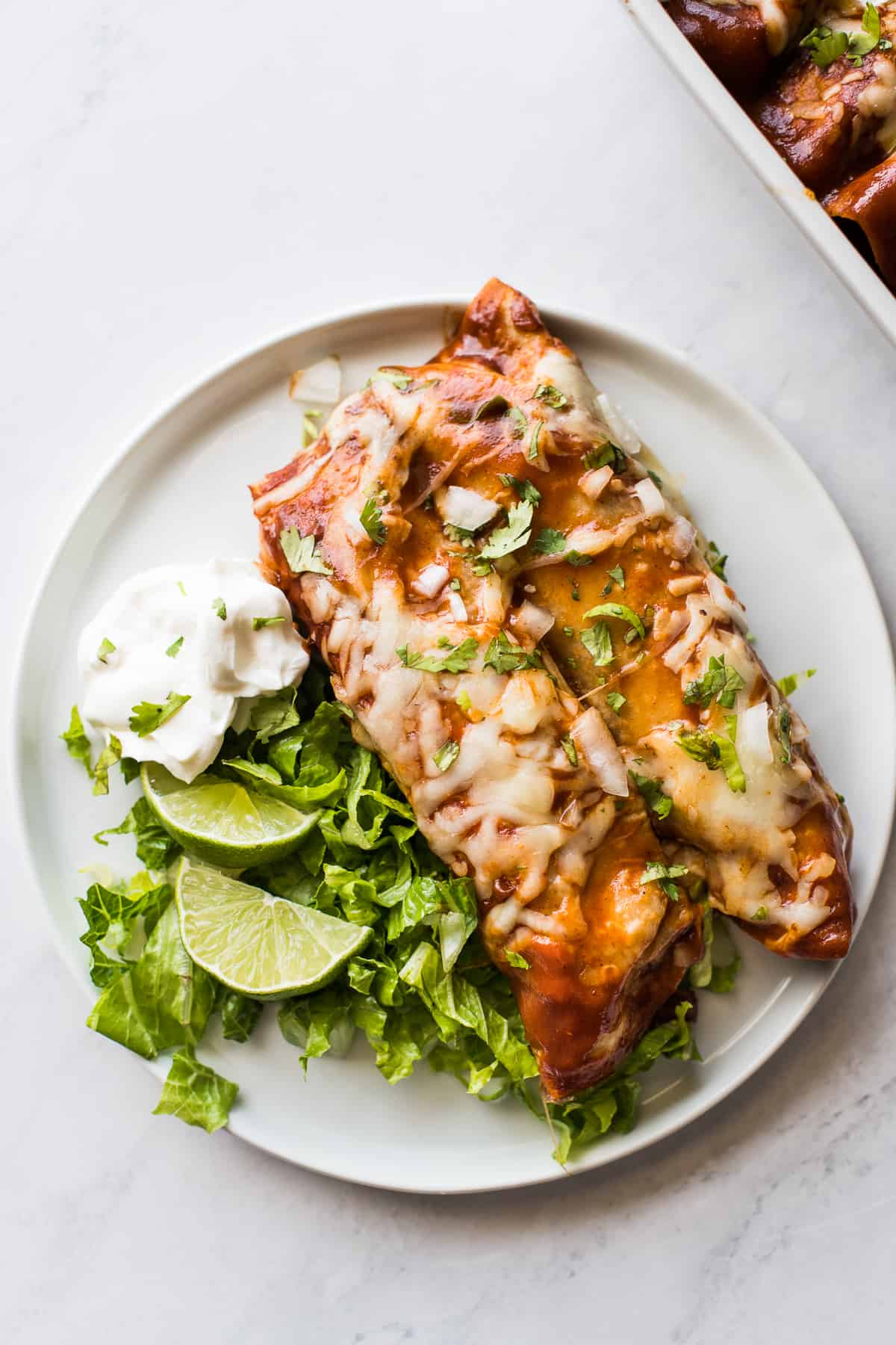 Two turkey enchiladas on a plate with limes, lettuce, and sour cream