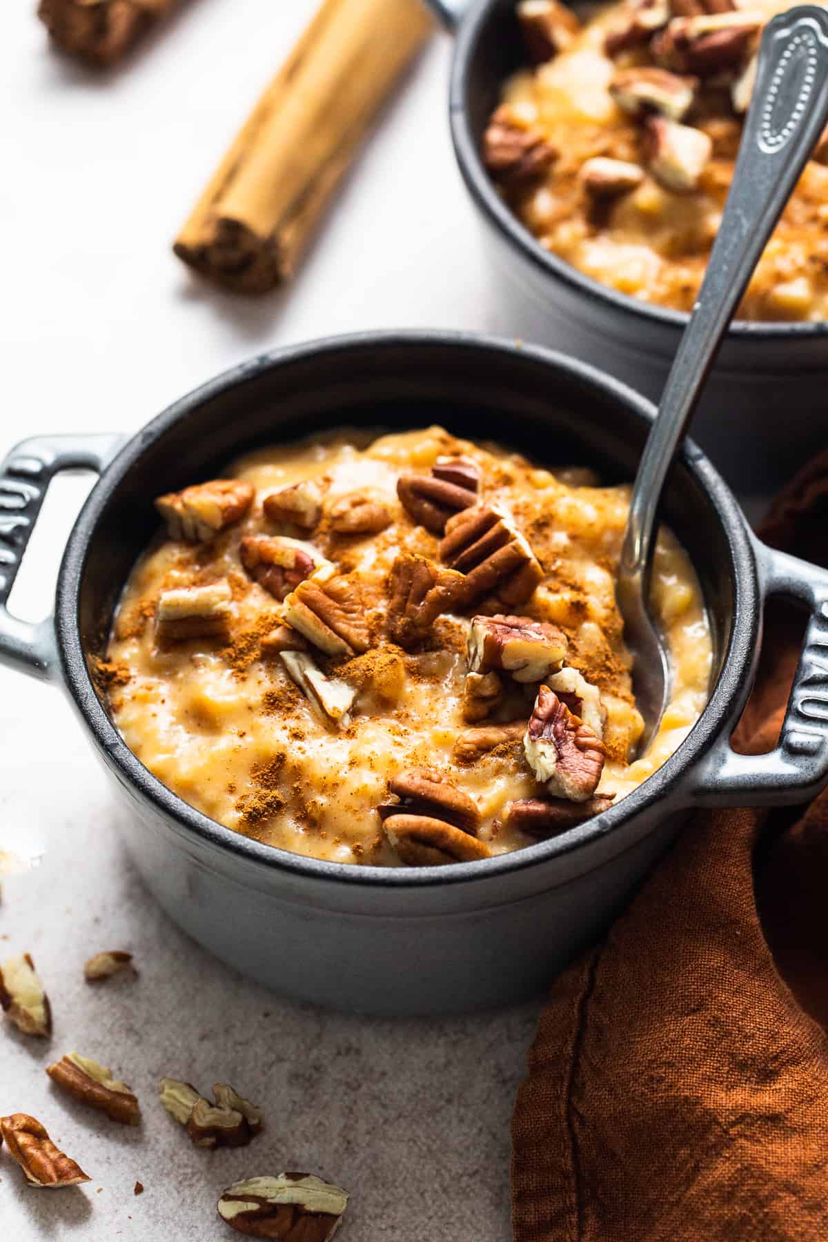 Pumpkin arroz con leche in a bowl topped with chopped pecans and ground cinnamon.