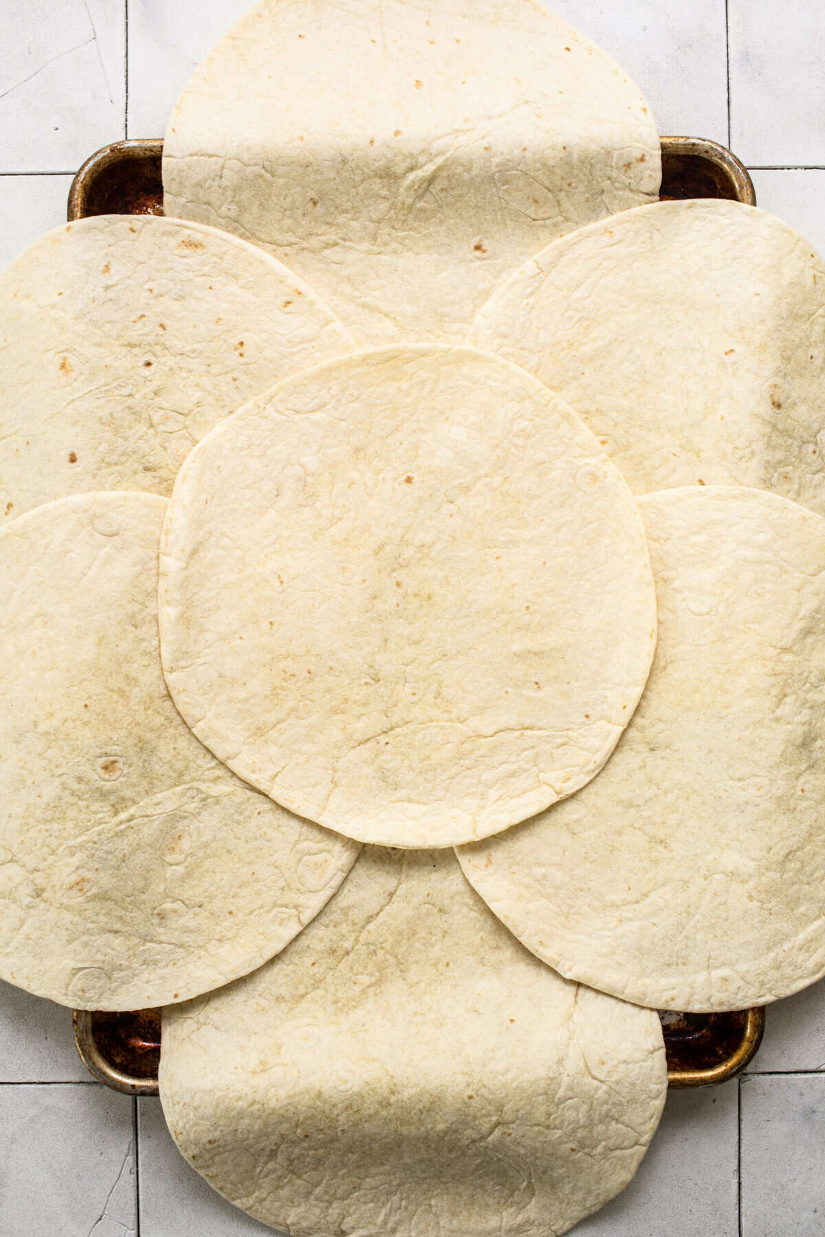 Flour tortillas laying on a sheet pan.