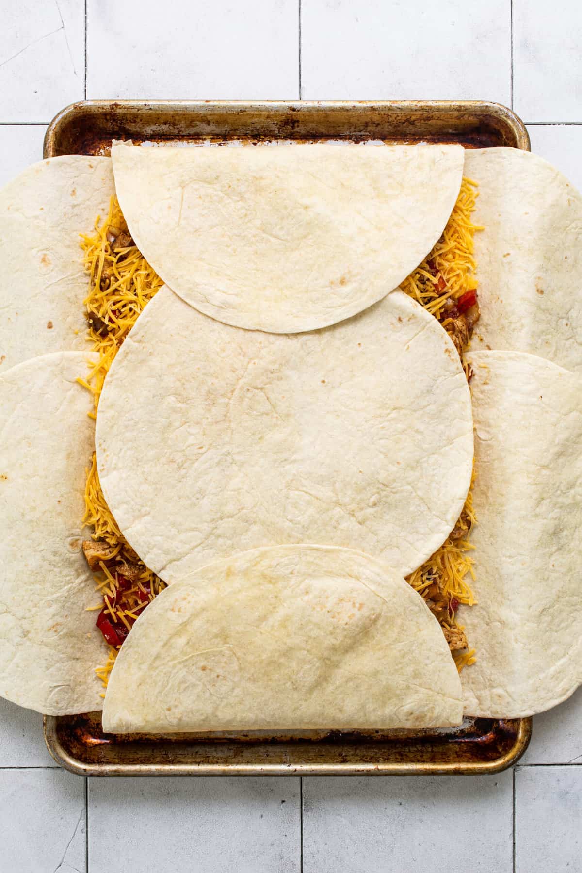 Large flour tortillas arranged on a sheet pan and being folded.