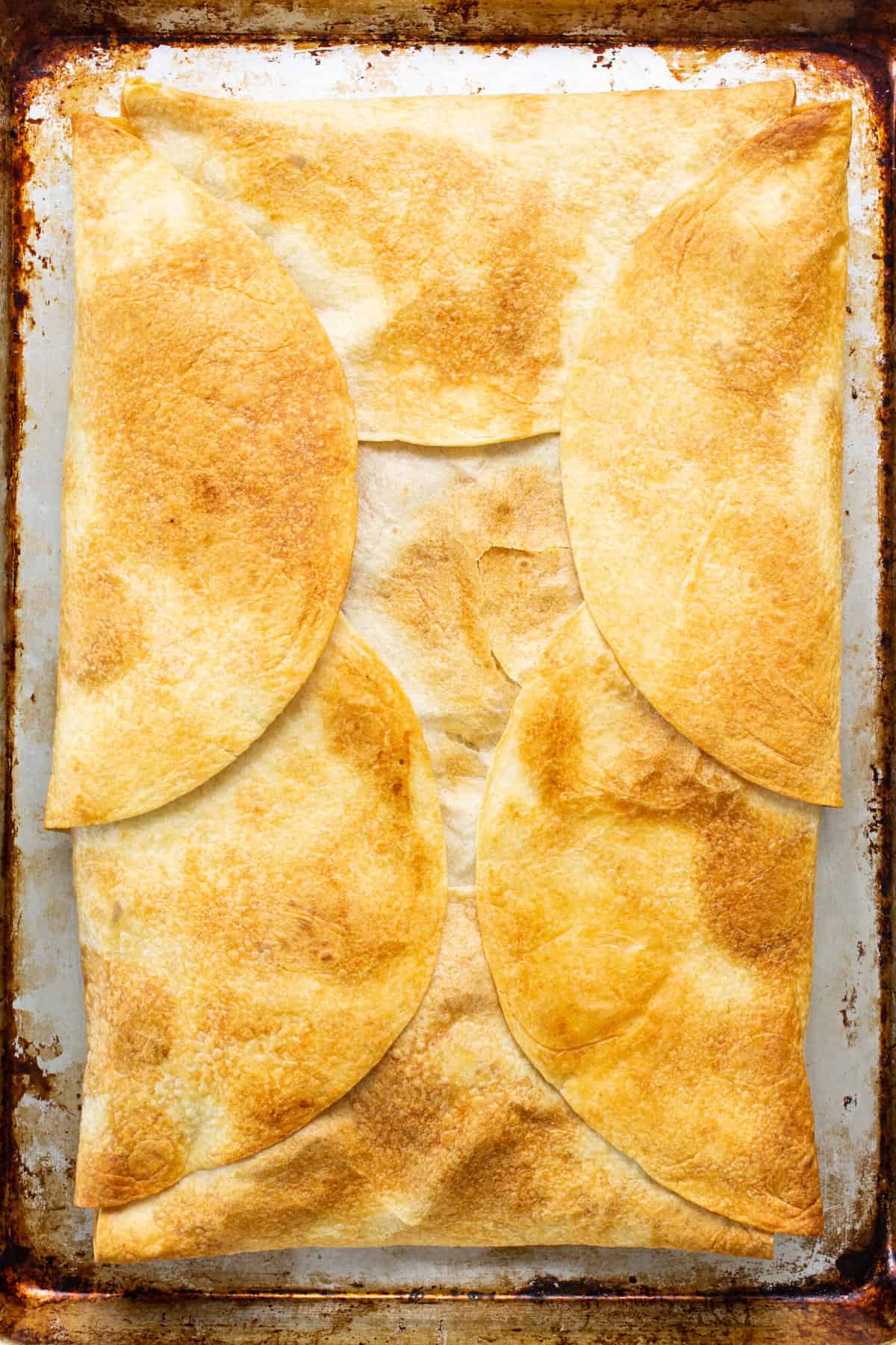 A golden crispy sheet pan quesadilla on a sheet pan before being sliced into individual servings.