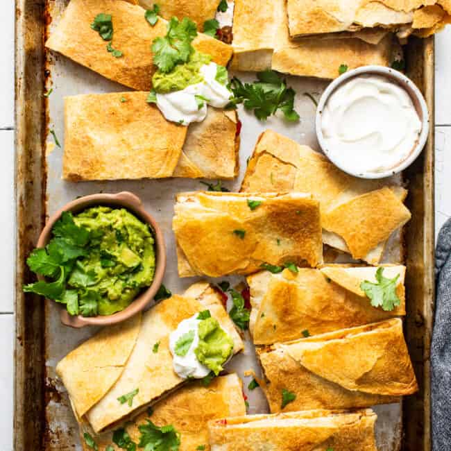 Sheet pan quesadillas on a sheet pan served with sour cream and guacamole.