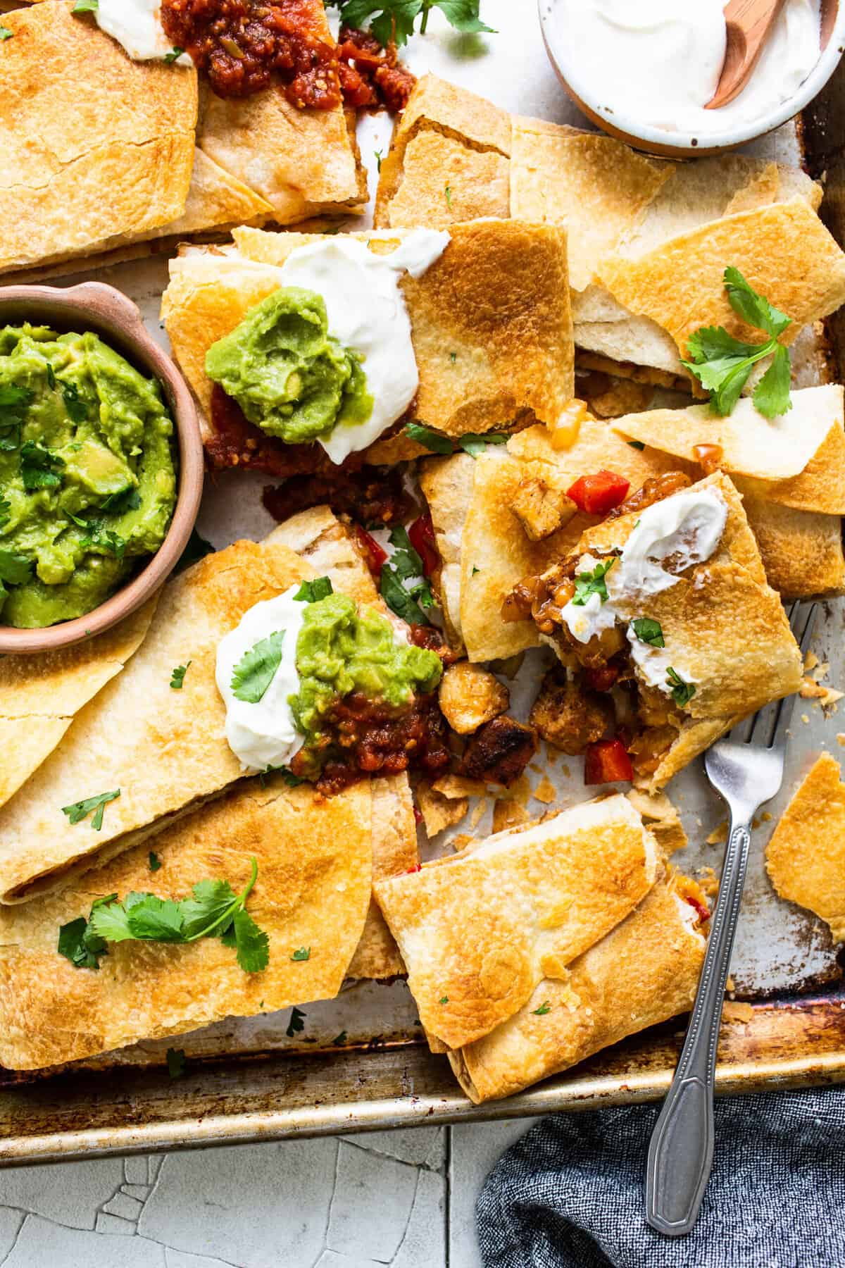 Sheet pan quesadillas sliced into pieces with sour cream and guacamole on top.