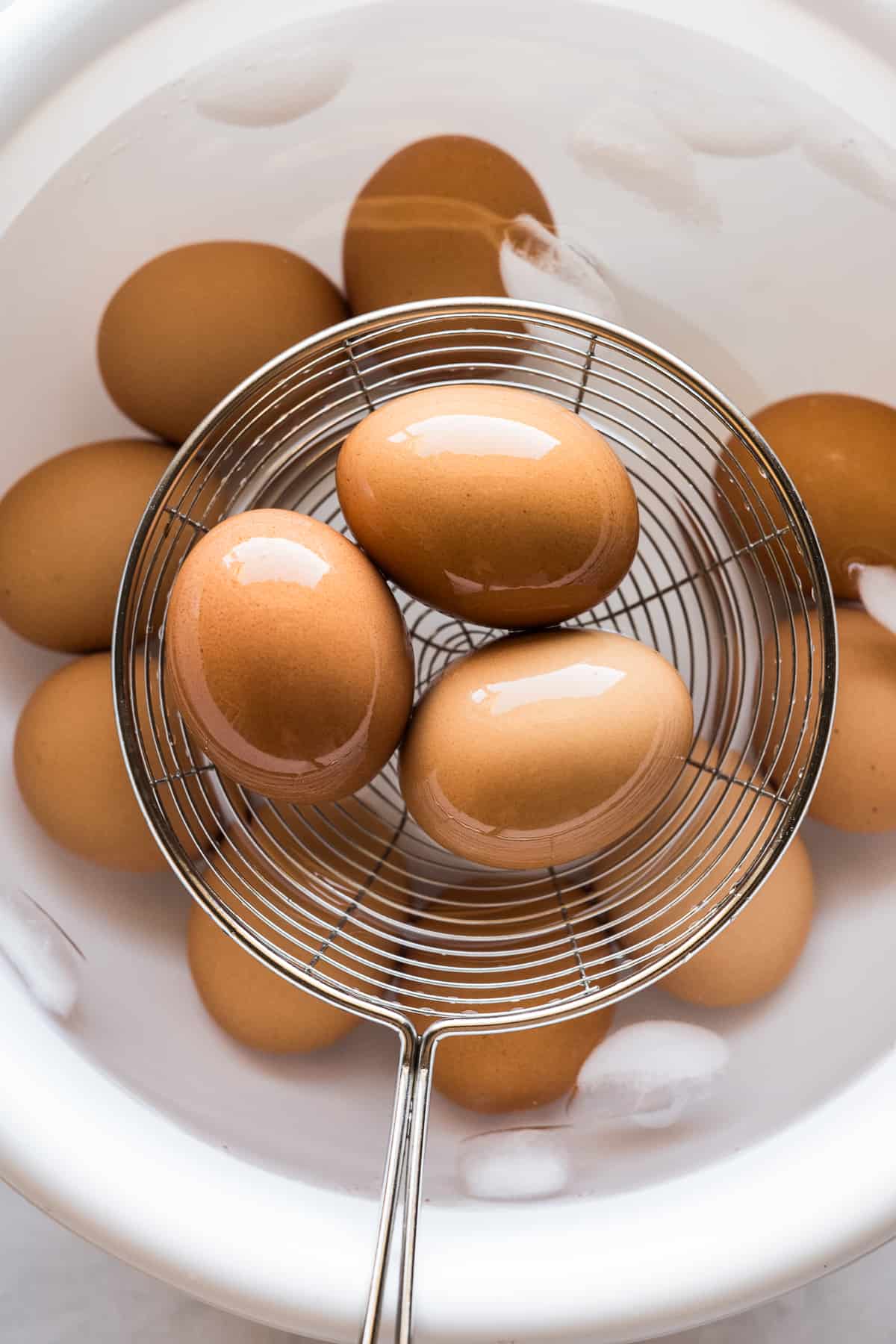 Eggs on a spider strainer coming out of bowl of ice water.