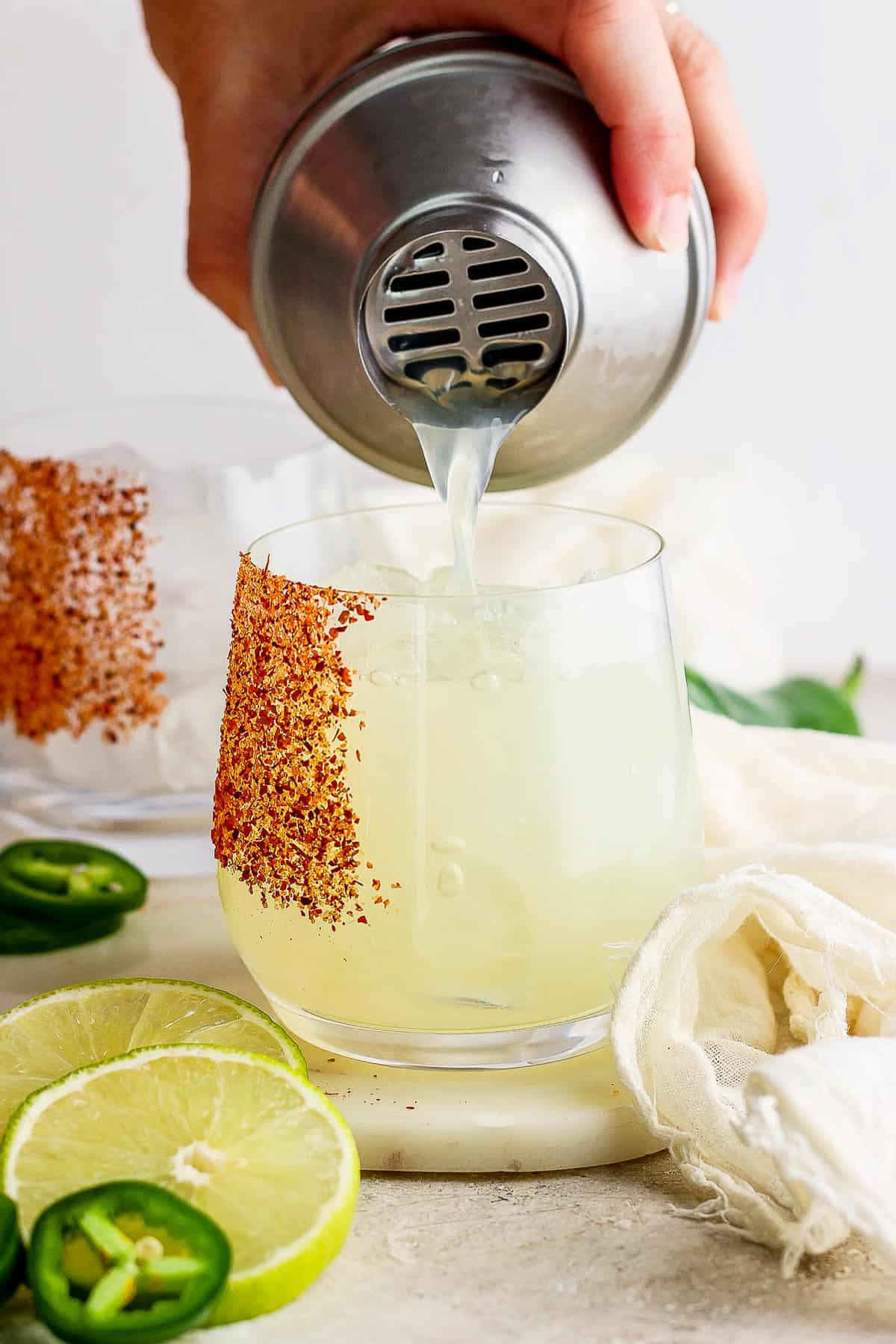 Straining a spicy margarita cocktail from a cocktail shaker into a glass.